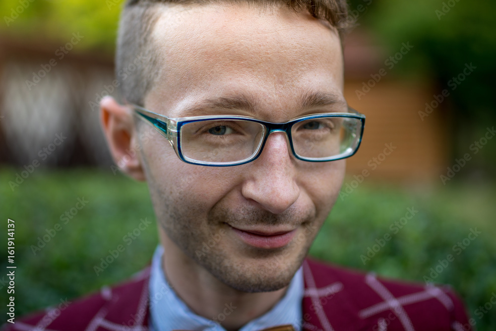 Portrait of a stylish young man wearing glasses plaid suit and a wooden bow tie. The man is smiling.close-up Portrait of a stylish young man wearing glasses plaid suit and a wooden bow tie. The man is smiling.close-up