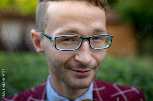 Portrait of a stylish young man wearing glasses plaid suit and a wooden bow tie. The man is smiling.close-up