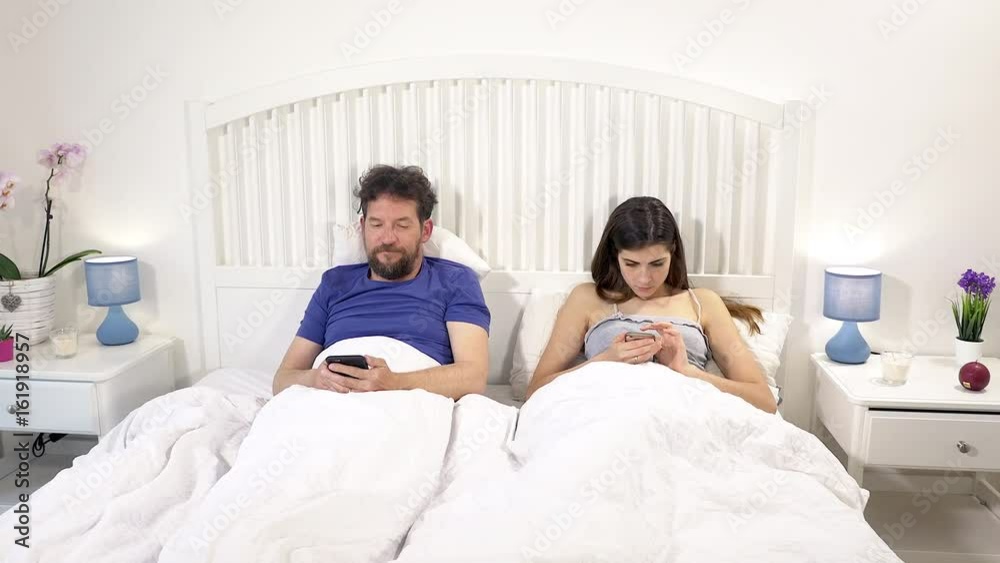 Modern times couple in bed not talking occupied with social network no love Modern times couple in bed not talking occupied with social network no love