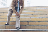 Businessman have the pain and painful knee expression and sit down on the stairs during go to office