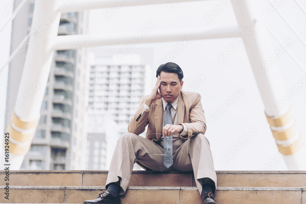 Tired businessman is holding on his head while sitting on the staircase,having a hard time with some ideas.