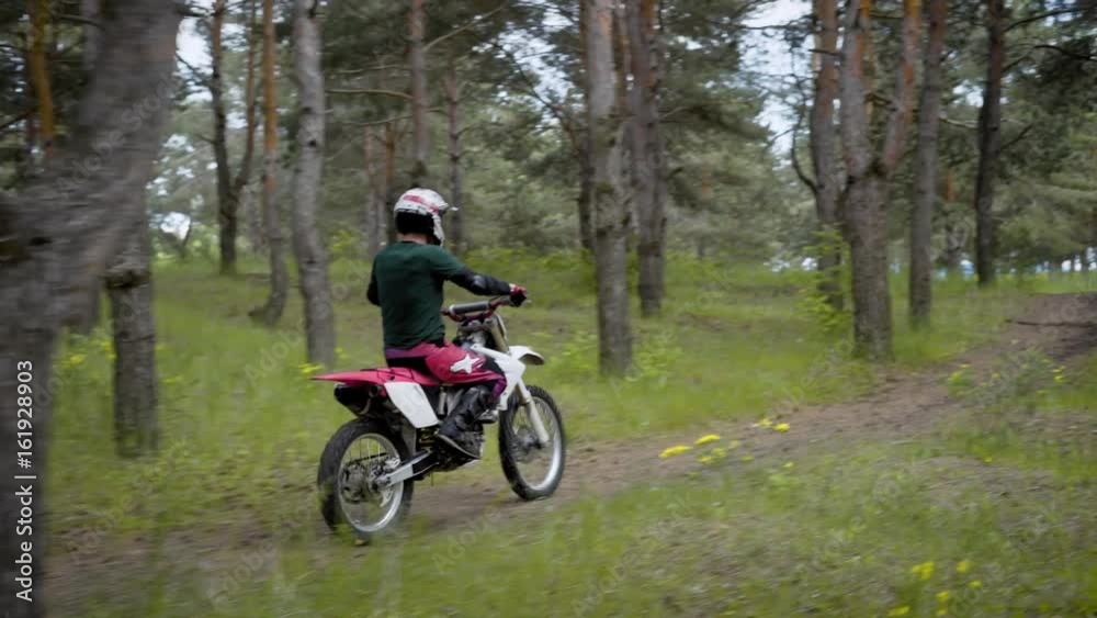 A motorcyclist in a protective helmet at a uniform is riding along a country road through a forest on a vehicle A motorcyclist in a protective helmet at a uniform is riding along a country road through a forest on a vehicle