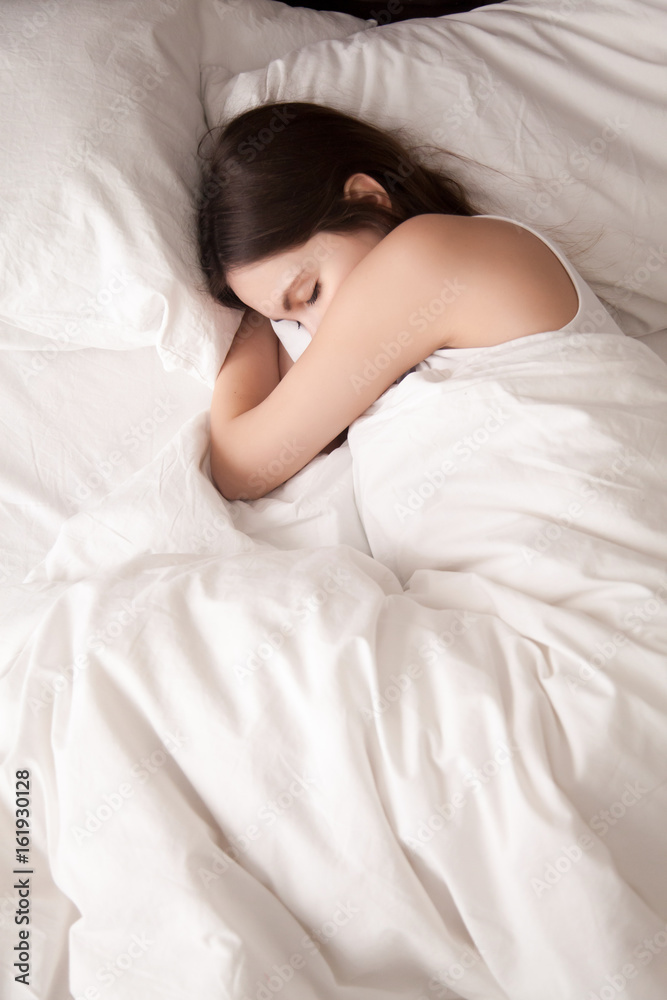 Fotografia do Stock: Tired young woman sleeping well on the side in bed  with white sheets, resting after sleepless night. Female student lying in  bed until late morning. Getting enough sleep concept.