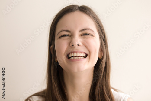 Headshot portrait of laughing young woman. Cheerful teen girl with happy facial expression looking at camera with toothy smile. Female positive emotion, comic situation concept. Close up. Front view