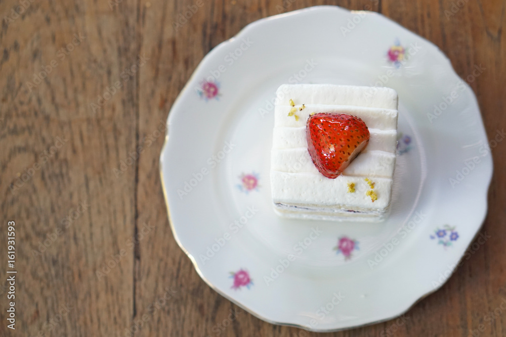 Homemade strawberry cake and cream topped with fresh strawberry on wooden table background.