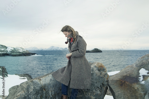 Woman with pipe in mouth leaning on boulder by sea photo