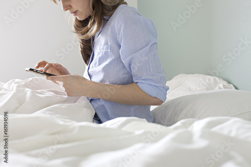 Brownhaired girl checking her phone from bed in pyjamas photo