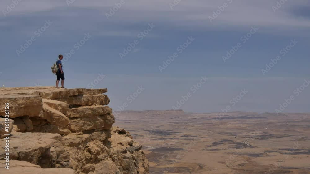 Man with backpack standing on the desert mountain rock cliff edge