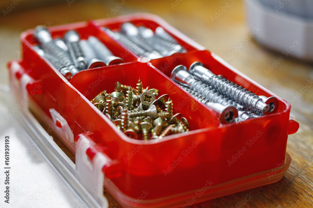 Set of fasteners for assembling furniture in a red plastic storage box on a wooden table Set of fasteners for assembling furniture in a red plastic storage box on a wooden table