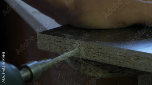 Man holds a drill in his hands and makes a hole in a wooden board. Wood shavings flying around. Close up, slow motion photo