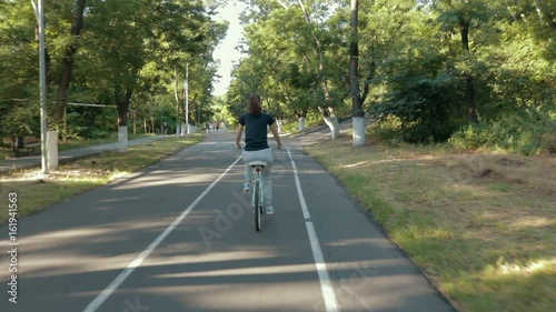 Wallpaper Mural Young slim woman rides a bicycle on a sunny day. Back view, slow motion. Torontodigital.ca