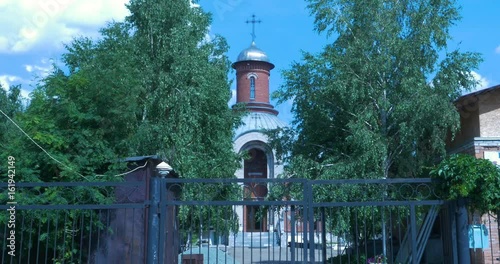 Orthodox temple orange brick with sunny ray, flowering green trees in foreground. Blue sky white clouds. Pray, holy light new christ church. Summer time, sunny day photo