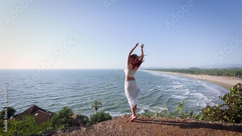 Woman in white dress dancing over the ocean opposite the sea waves and the beach. India, Gokarna.