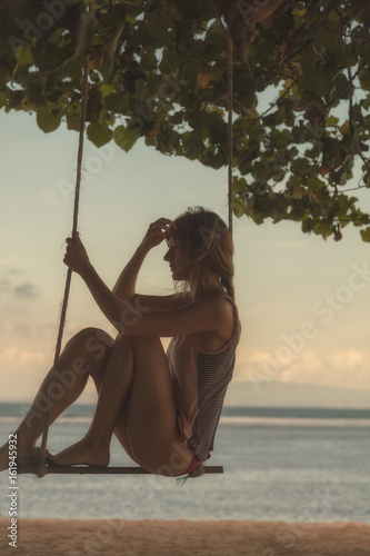 Girl swinging on a sandy beach with ocean / sea view.