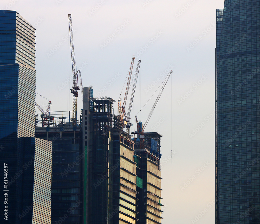 Construction of a highrise building in Singapore with cranes and scaffolding