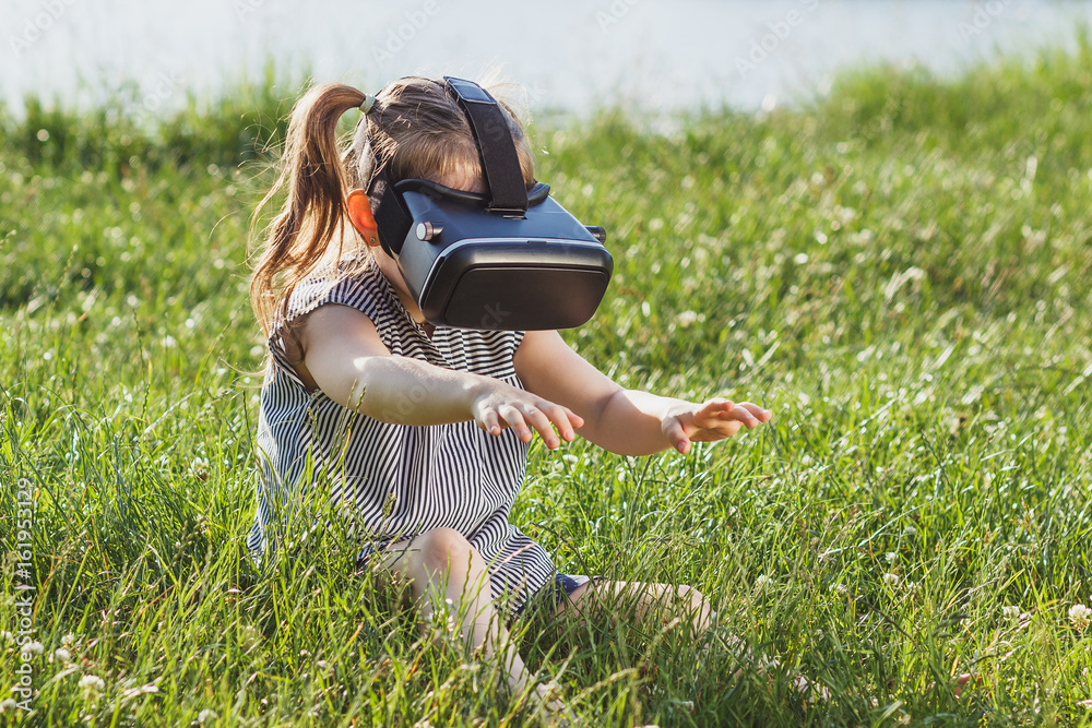 Fototapeta premium Little girl plays game with virtual reality glasses outdoors