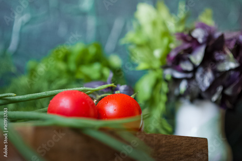 Ripe juicy tomatoes with droplets of water on a dark background in a wooden box with a sprig. Greenery, basil, arugula, onion, parsley, dill. Vitamins, greens, vegetarianism, healthy food, sports.