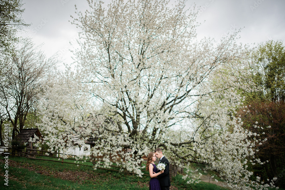Stunning couple stands under large white tree with white flowers
