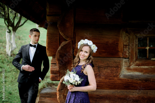 Young man watches pretty brie in white wreath and violet dress