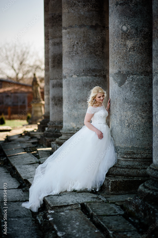 Obraz premium Blonde bride leans to an old stone column