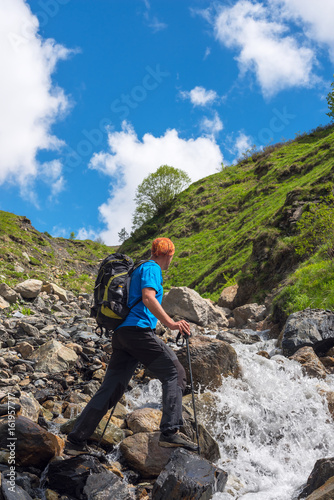Man adventurer with backpack is preparing to jump over a mountain river
