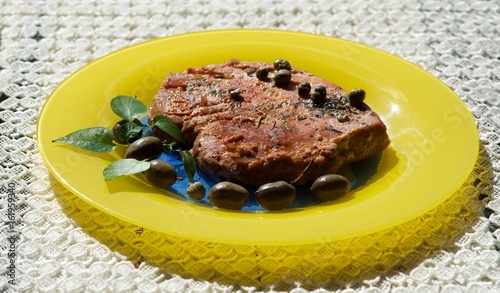Tuna steak served with olives, basil and capper in yellow plate in blurry background. Maltese cuisine. Healthy food photo