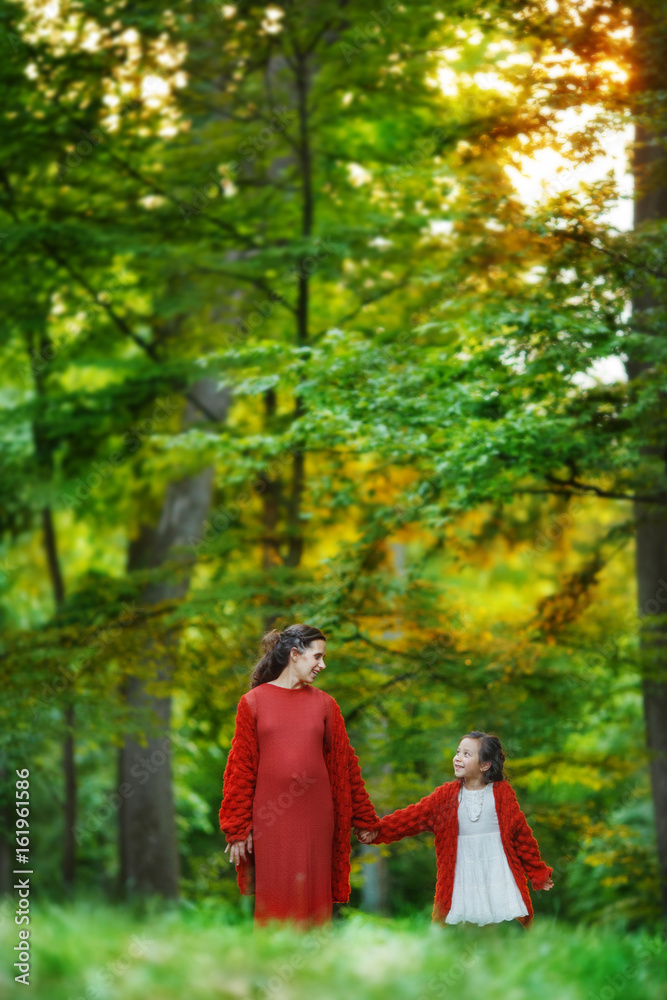 A pregnant woman and her eldest daughter are walking alone along the lush green spring forest, holding each other's hands.