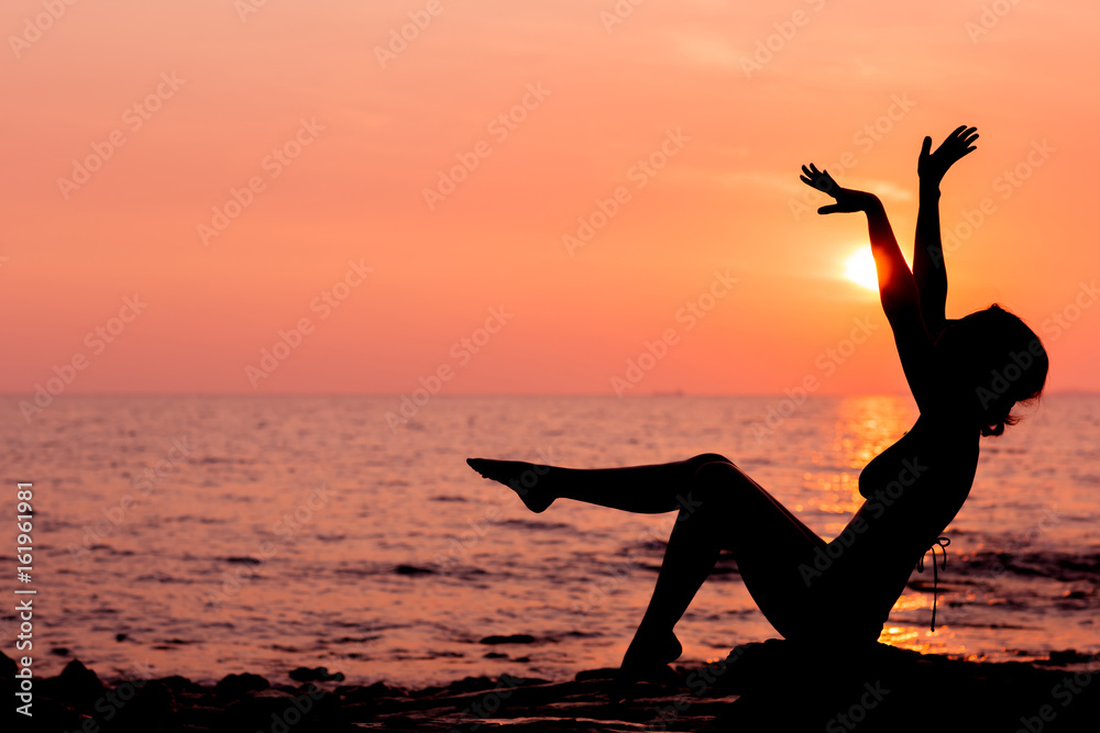 Woman silhouette sitting on sunset sea background, side view, back lit