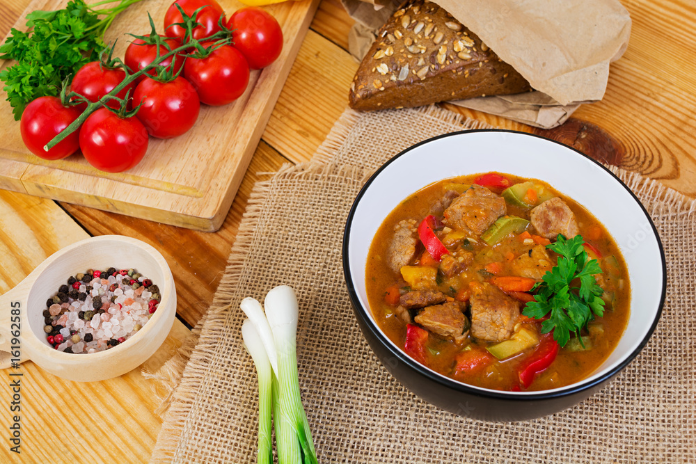 Stew with meat and vegetables in tomato sauce on wooden background Stew with meat and vegetables in tomato sauce on wooden background