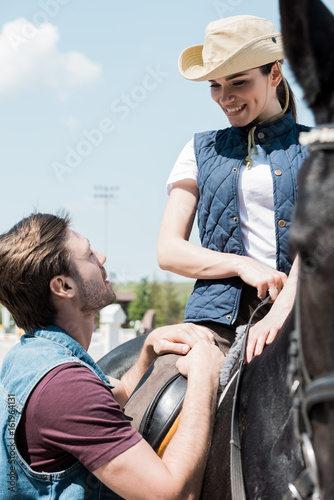 Handsome young man looking at smiling woman sitting on horseback