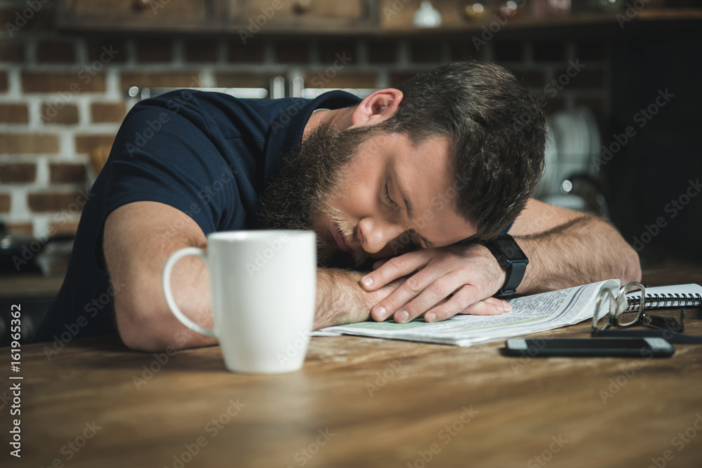 Obraz premium portrait of tired man sleeping on table with newspaper and coffee cup