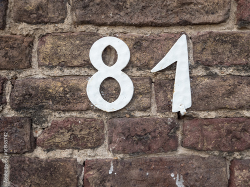 White house number 81 on an old brick wall