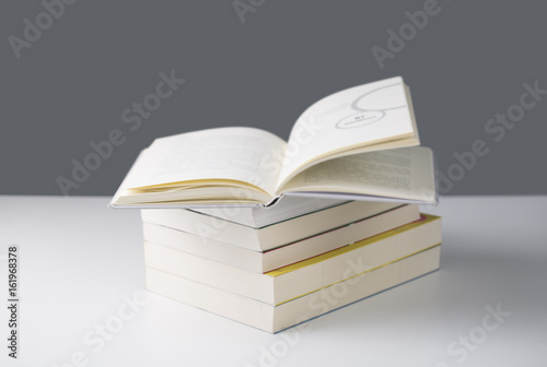 Pile of books with one book open on white table.