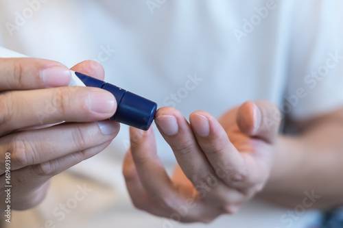 Medicine  diabetes  glycemia  health care and people concept - close up of man hands use lancet on finger to checking blood sugar level by Glucose meter