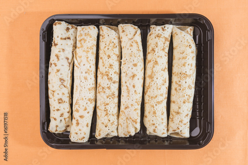 Pancakes rolls with a filling lie in a dark brown tray on a gentle peach-orange background