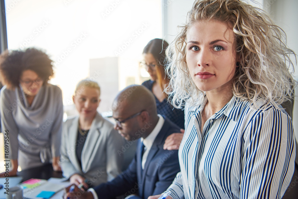 Focused young businesswoman with colleagues working in the background