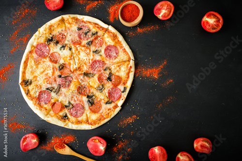 Frame of tasty Italian pizza with ingredients and spices on dark background. Flat lay, top view.