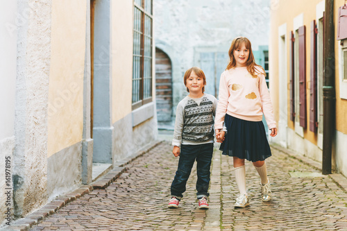 Outdoor portrait of adorable fashion kids, wearing sweatshirts, holding hands, walking together in a city