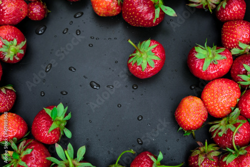 Red juicy strawberry on a dark black wooden background.The droplets of water. Juiciness, vitamins and healthy food. Place for print