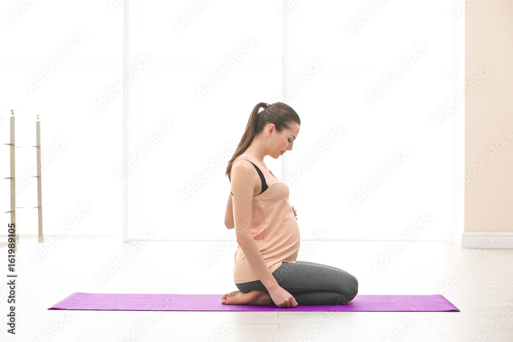 Fototapeta premium Beautiful pregnant woman doing exercise indoors
