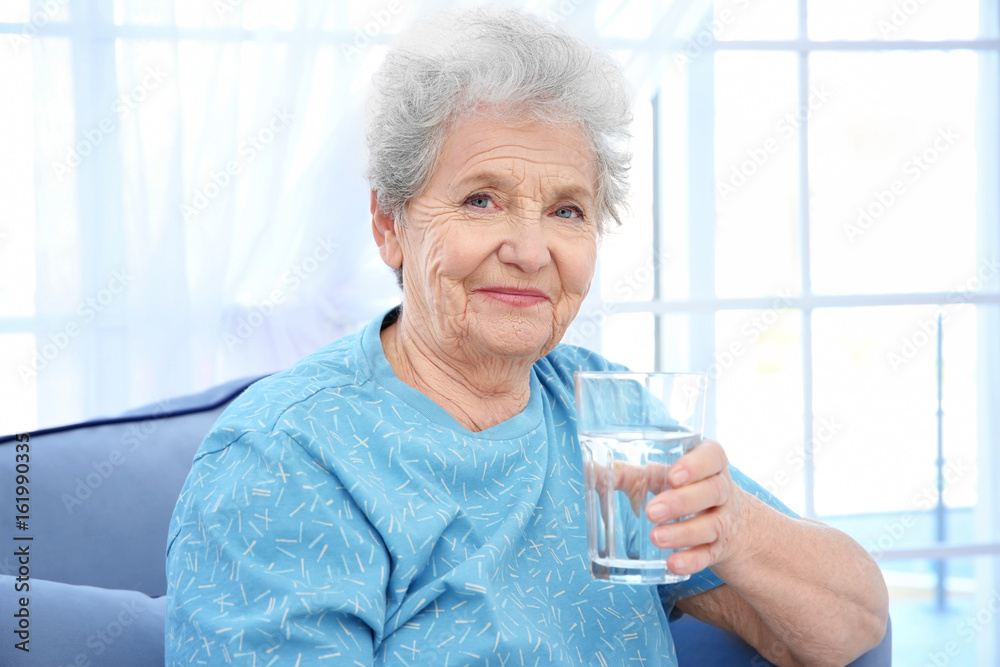 Elderly woman sitting on couch and holding glass of water. Concept of retirement Elderly woman sitting on couch and holding glass of water. Concept of retirement