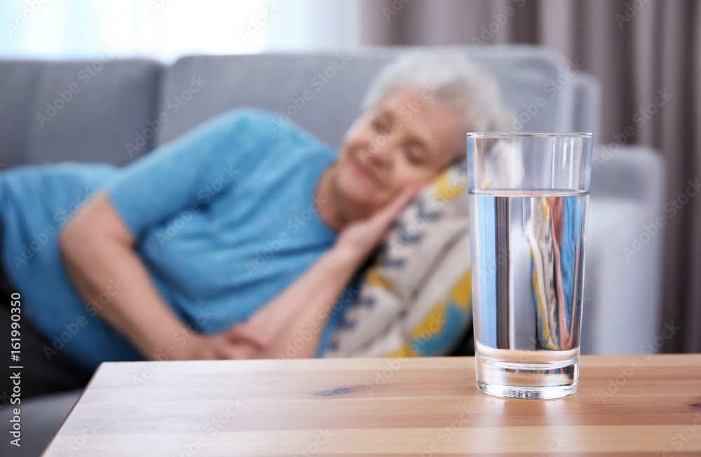 Glass of water on table and sleeping elderly woman at home. Concept of retirement Glass of water on table and sleeping elderly woman at home. Concept of retirement
