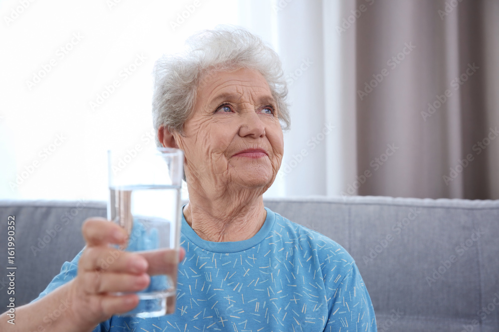 Elderly woman sitting on couch and holding glass of water. Concept of retirement Elderly woman sitting on couch and holding glass of water. Concept of retirement