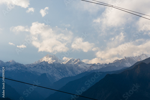 Kangchenjunga mountain with clouds above. Among green hills and house with electric cable that view in the evening in North Sikkim, India.