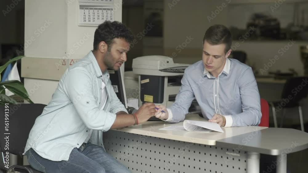 Swarthy guy signs a documents about buying a car in car showroom Swarthy guy signs a documents about buying a car in car showroom