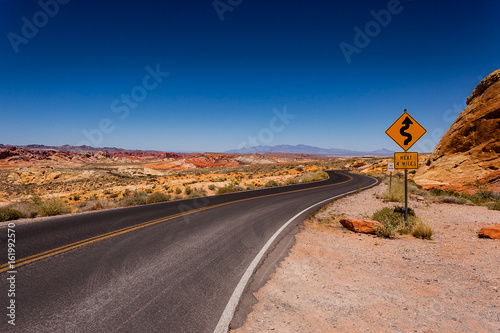 Long winding road with road sign leading to mountains in distance