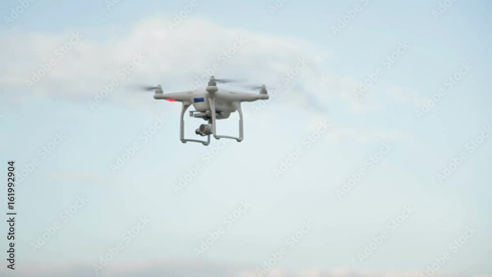 White drone quadcopter flying in the blue sky White drone quadcopter flying in the blue sky