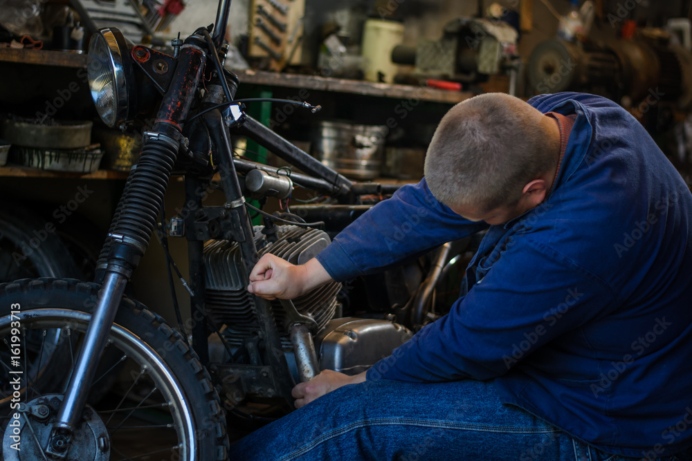 Man with tools repairing old motorcycle in workshop Man with tools repairing old motorcycle in workshop