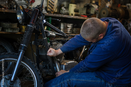 Man with tools repairing old motorcycle in workshop