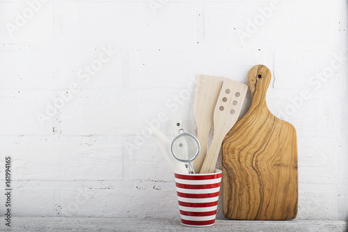 A simple kitchen still life against a white brick wall: cutting board, cooking equipment, ceramics. Horizontal photo